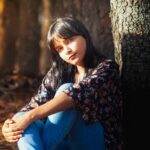 A serene portrait of a young woman sitting in a sunlit autumn forest, capturing nature's tranquility.