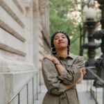 Confident woman in fashionable outfit posing outdoors against an urban architectural backdrop.