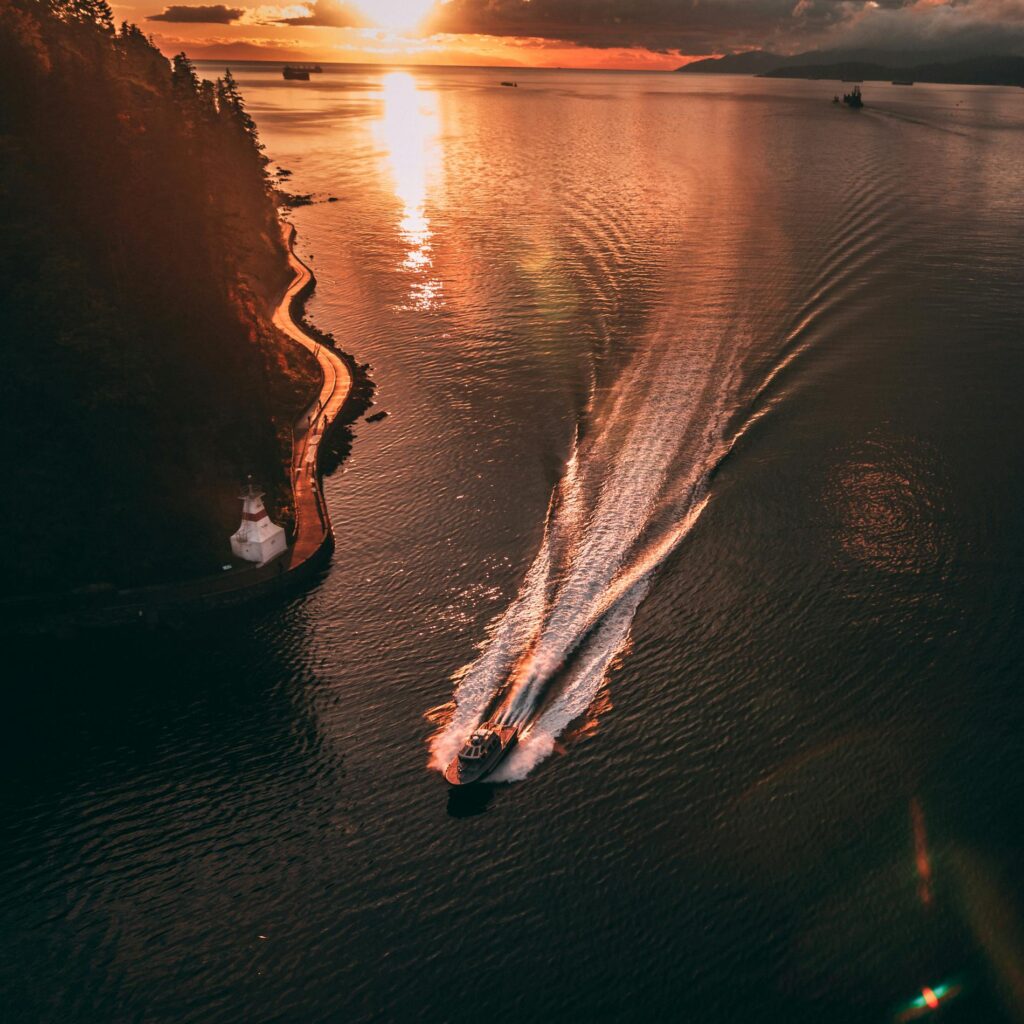 A scenic aerial view of a boat cruising through coastal waters at sunset with vibrant reflections and mountainous backdrop.